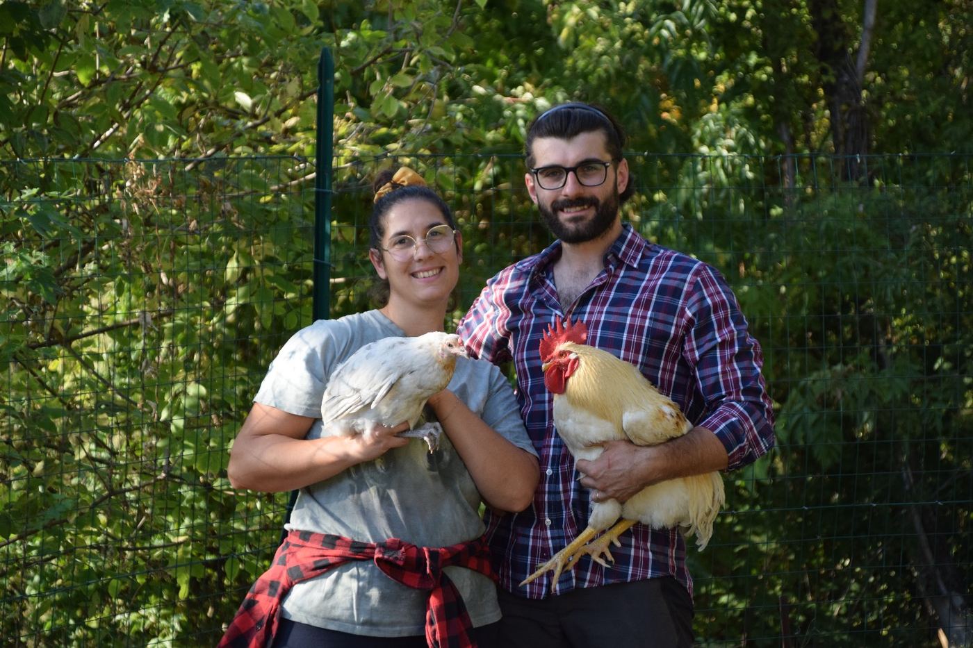Eleonora e Valentin sorridenti con in braccio una gallina e un gallo della fattoria